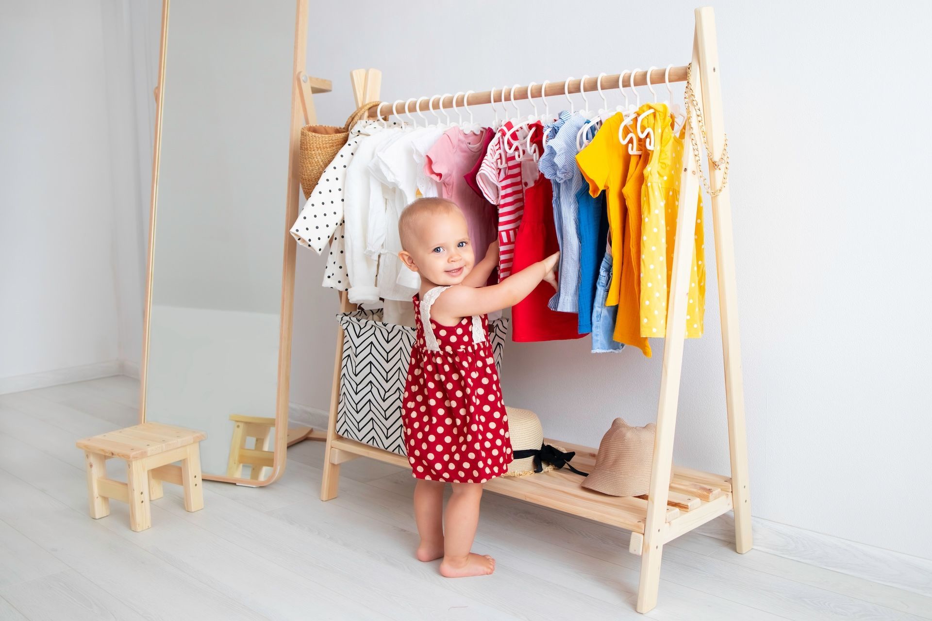Montessori Toddler chooses clothes from a wooden rack in a brightly lit room.