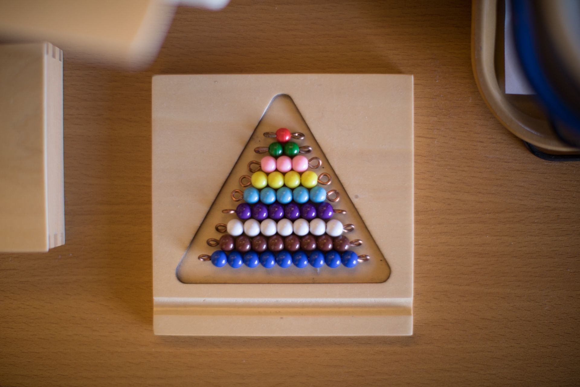 Wooden Montessori math board with colorful beads arranged in a triangular pattern.