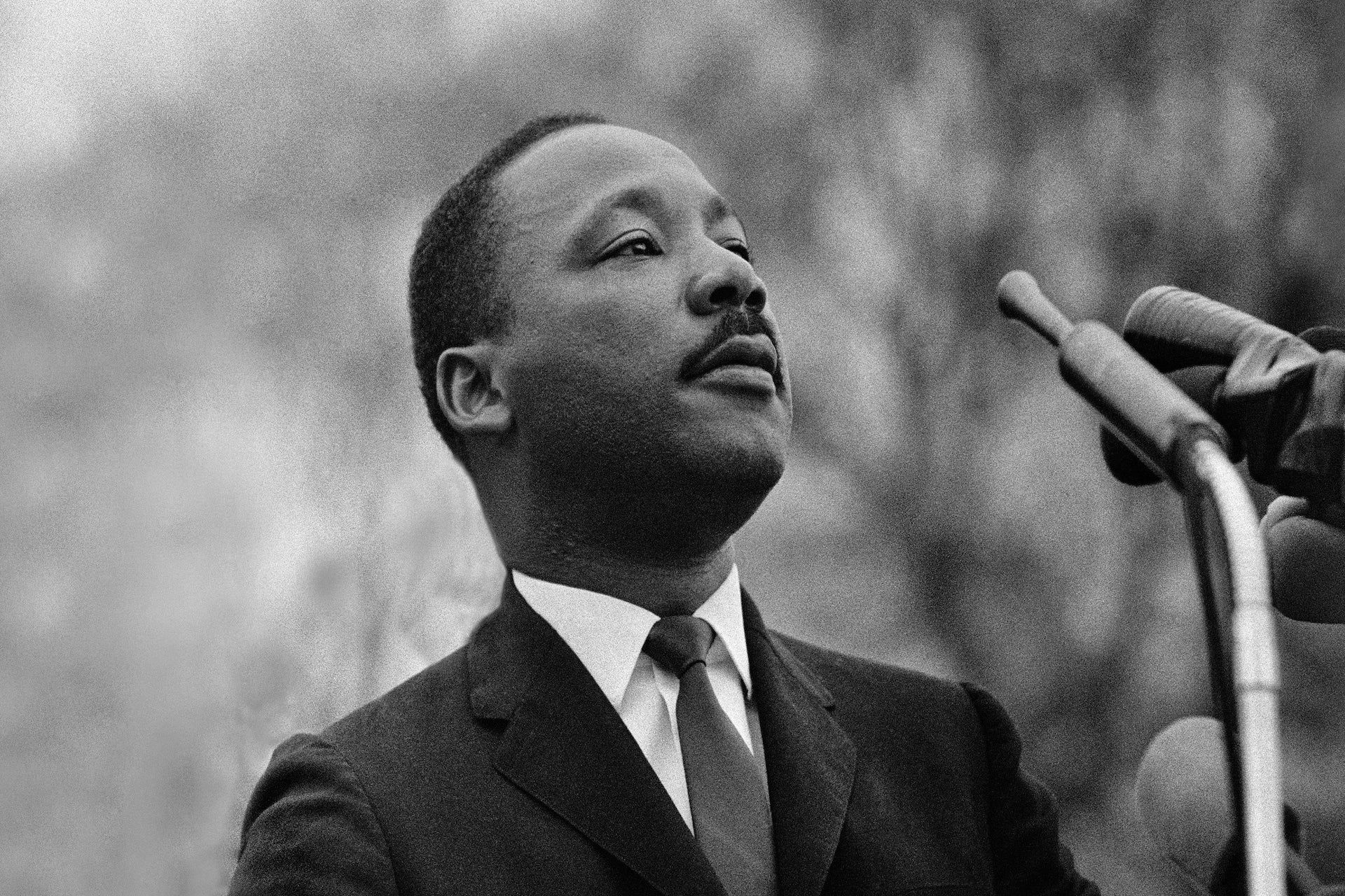 Martin Luther King Jr. speaking at a podium, looking up, with a pensive expression.