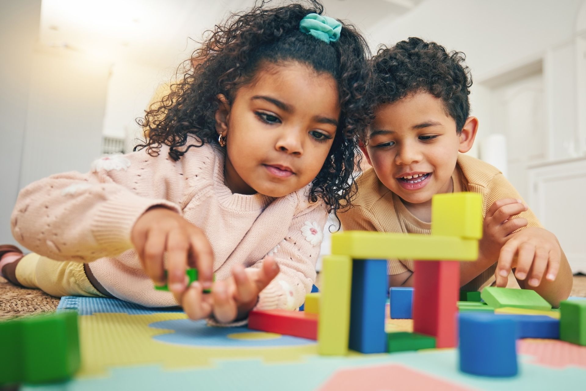 Two children building a colorful block structure on a playmat.