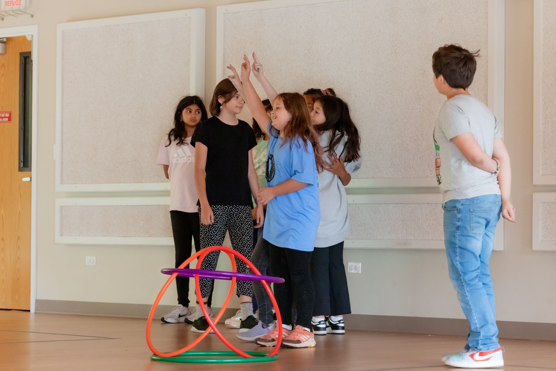 Group of kids playing a game with hoops. One boy watches. Indoors, neutral background.