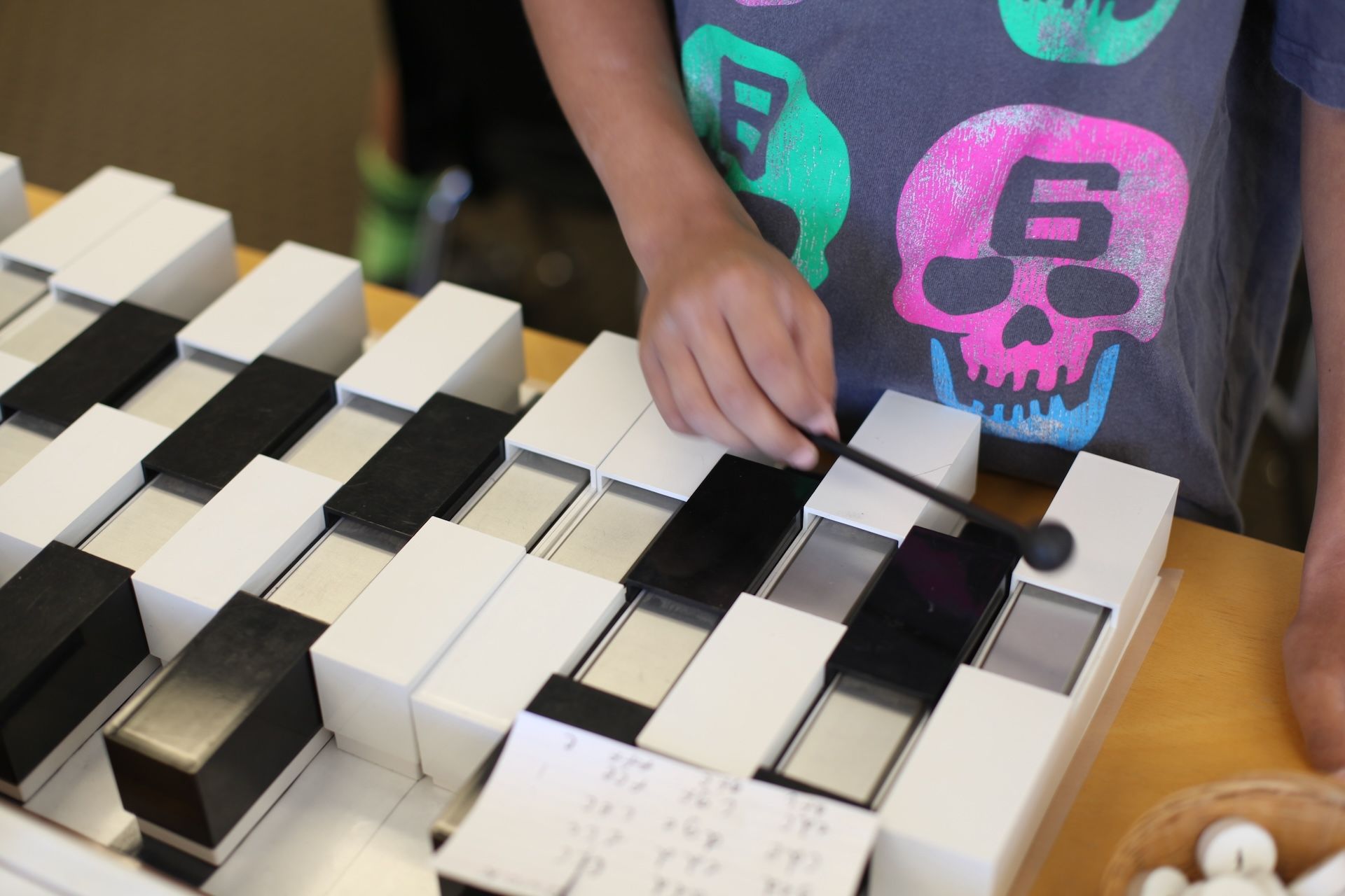 Child playing a wooden xylophone with a mallet. The instrument is made of black and white blocks.