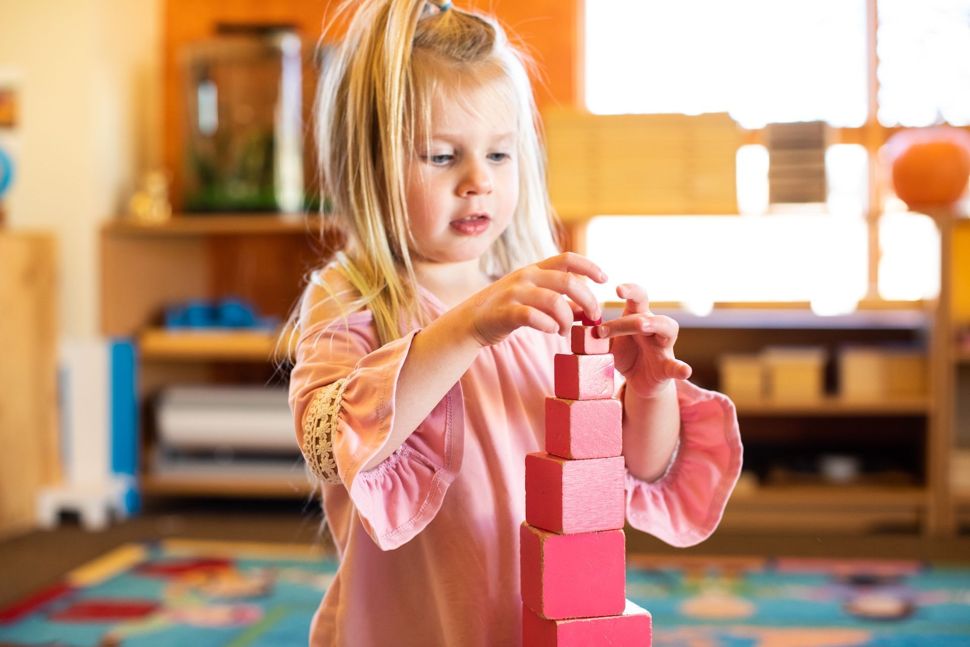 Child stacking pink blocks at a table in a bright classroom
