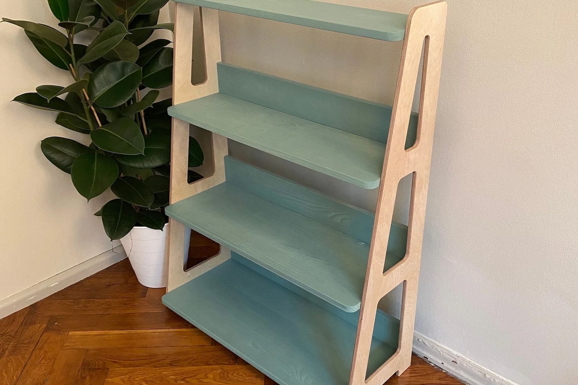 A blue-shelved bookshelf with white supports, in a corner next to a leafy plant.