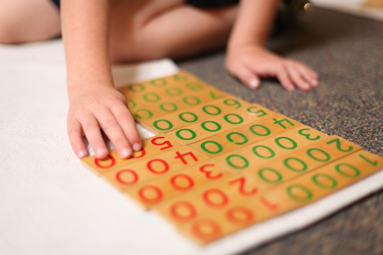 Child using Montessori decimal cards to explore quantity and place value through hands-on math work.