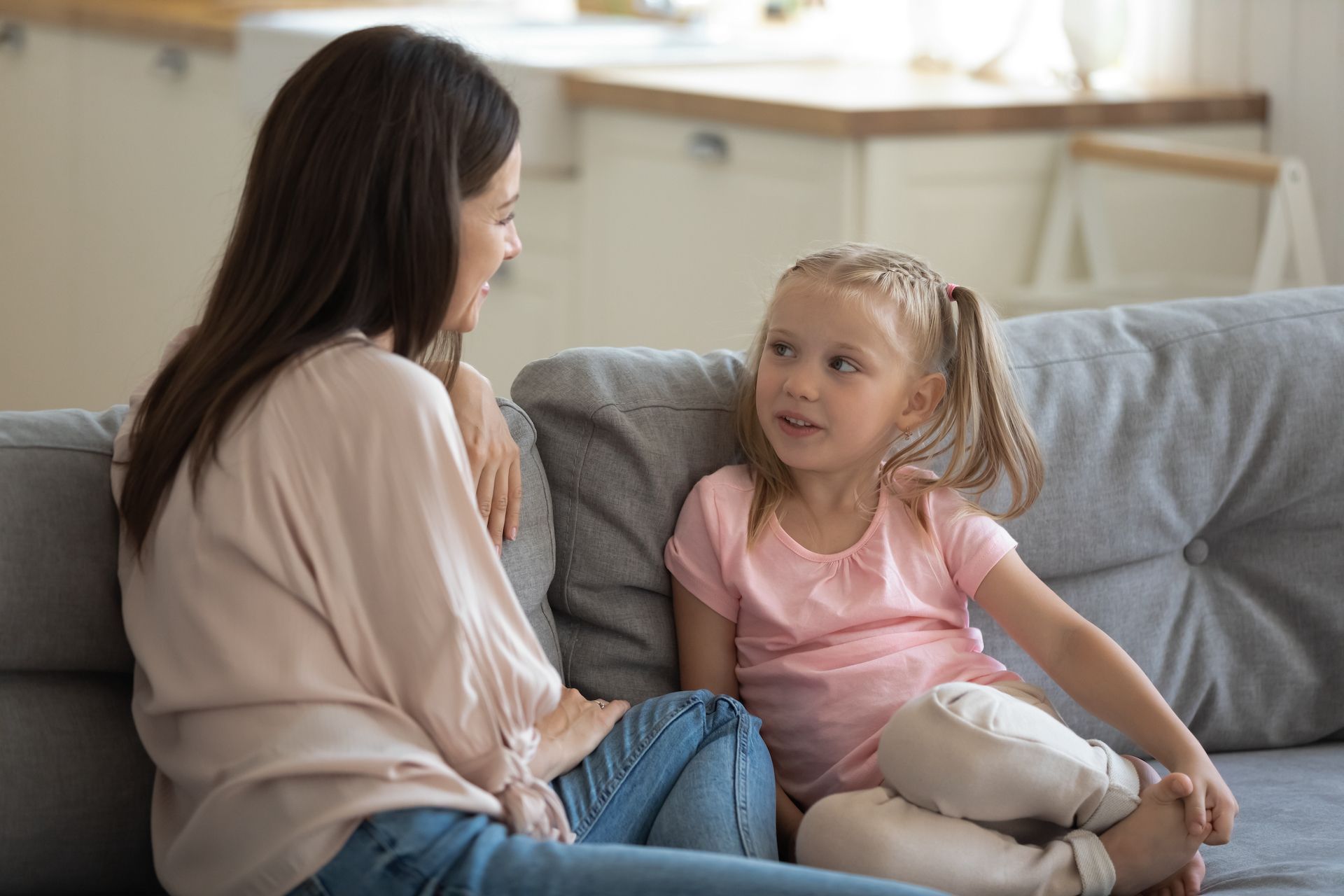 Mother and daughter sitting on couch, talking. The girl has pigtails.