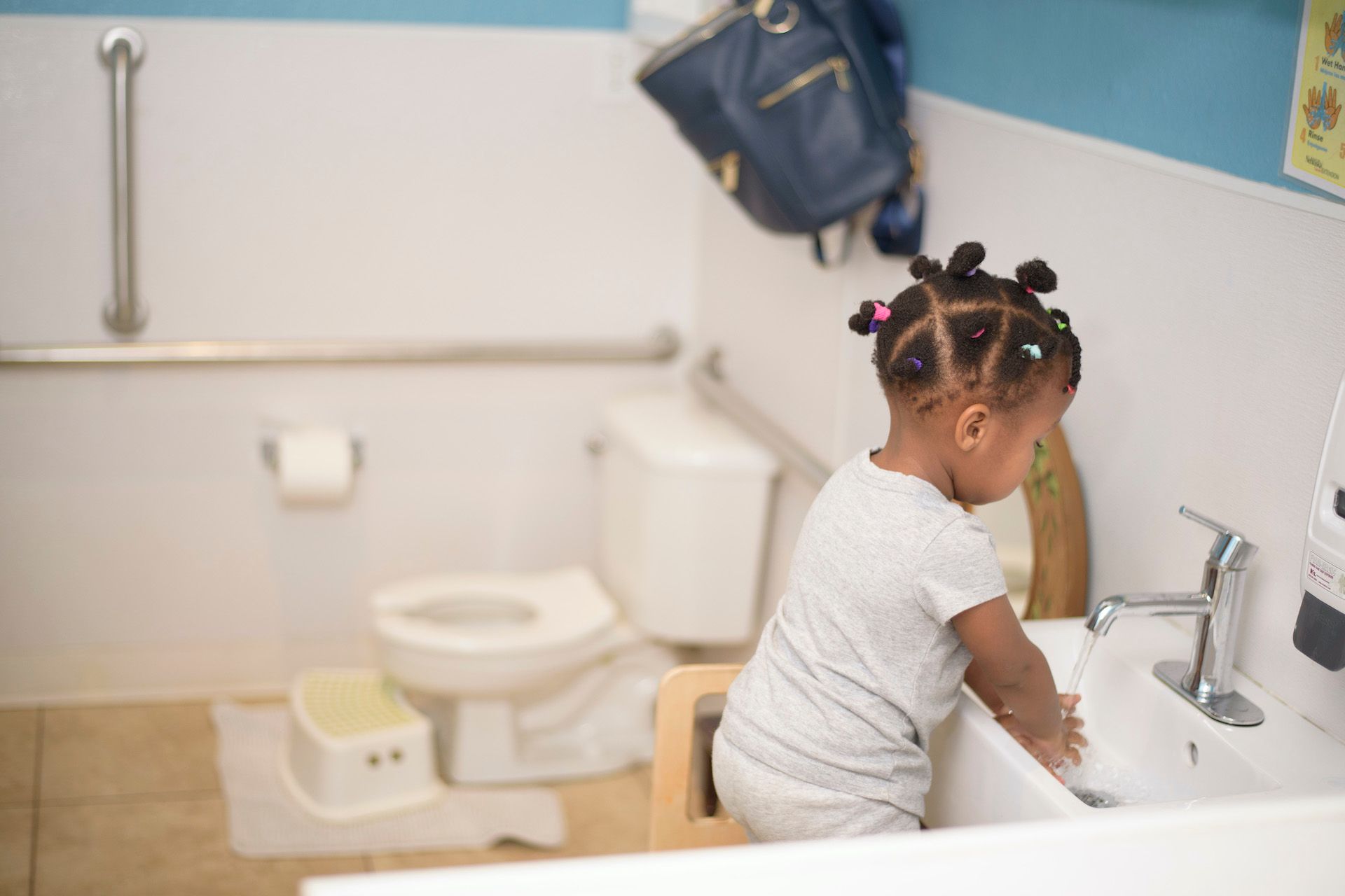 Young child washing hands in a small sink in a child-sized restroom.
