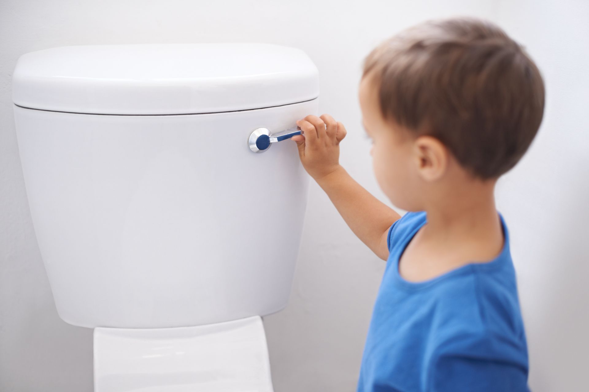 Young child in blue shirt pulling the toilet flush lever.