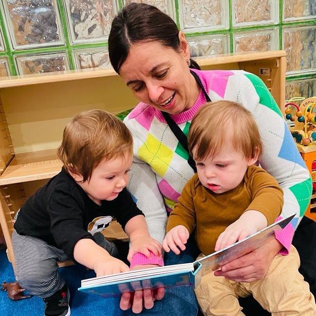 A montessori guide is reading a book to two young children.