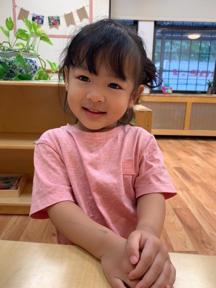 Smiling Montessori child at a wooden table in a classroom.