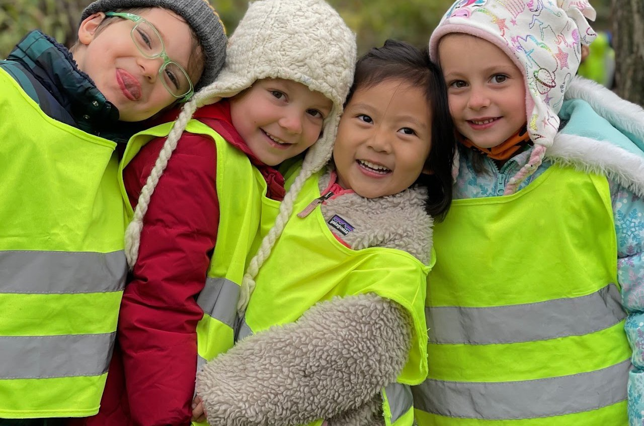 Four smiling children wearing reflective vests and winter hats outdoors.