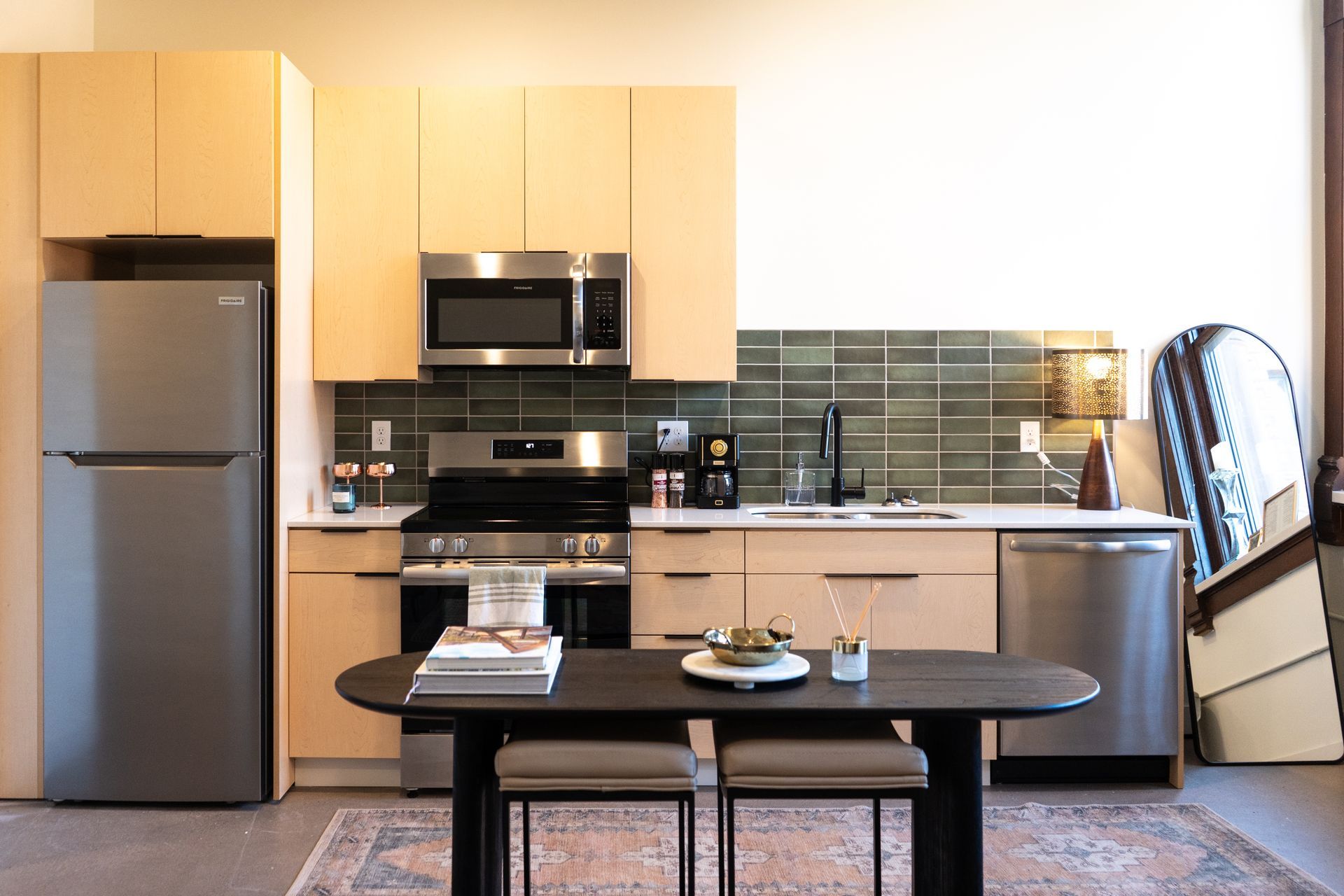 Modern kitchen with light wood cabinets, stainless steel appliances, and a dark table with two stools at Zenith Apartments in Duluth, MN.
