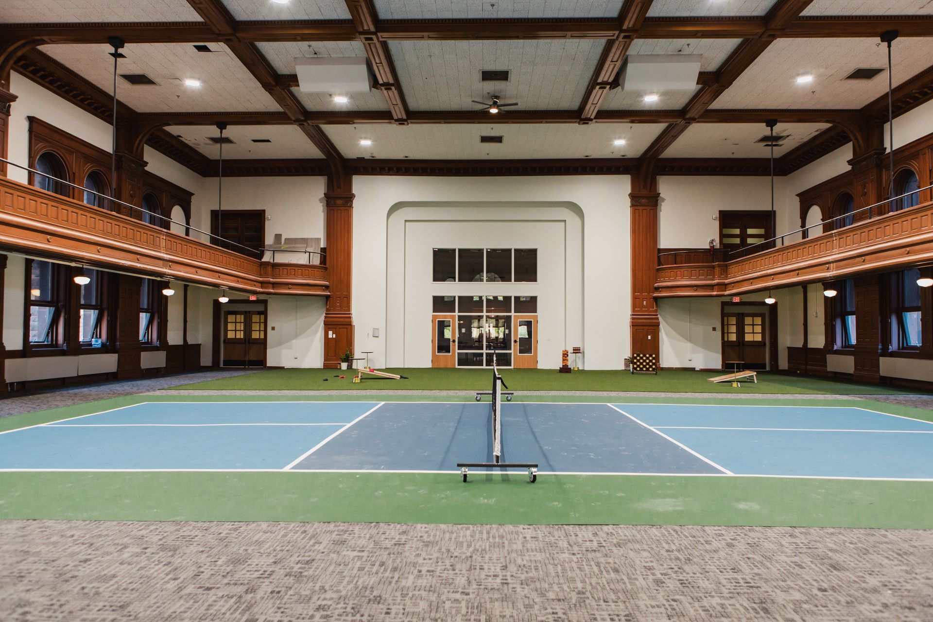 Indoor tennis court with blue and green surface, white lines, net. Red brick columns, balconies, wooden beams at Zenith Apartments in Duluth, MN.