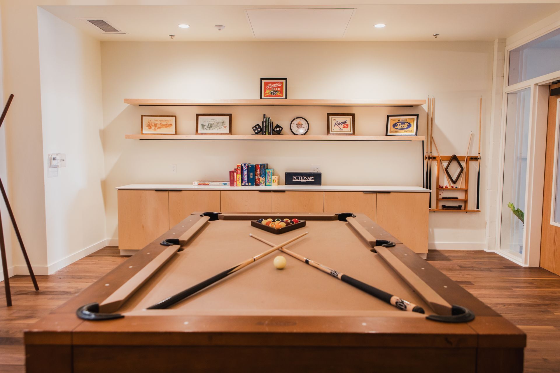 Pool table in a room with a light wood floor, shelves with decor, and a cabinet. Cue sticks crossed on the table at Zenith Apartments in Duluth, MN.