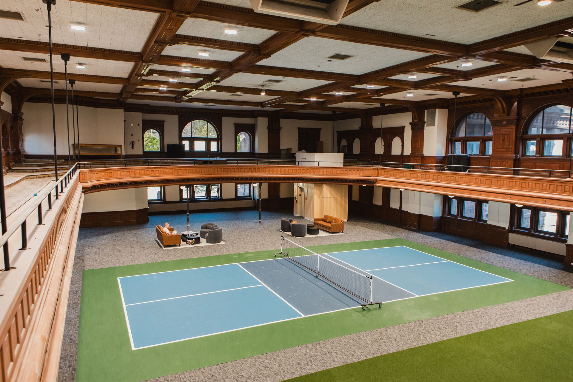 Indoor pickleball court with blue and green flooring, surrounded by a wood-paneled balcony at Zenith Apartments in Duluth, MN.