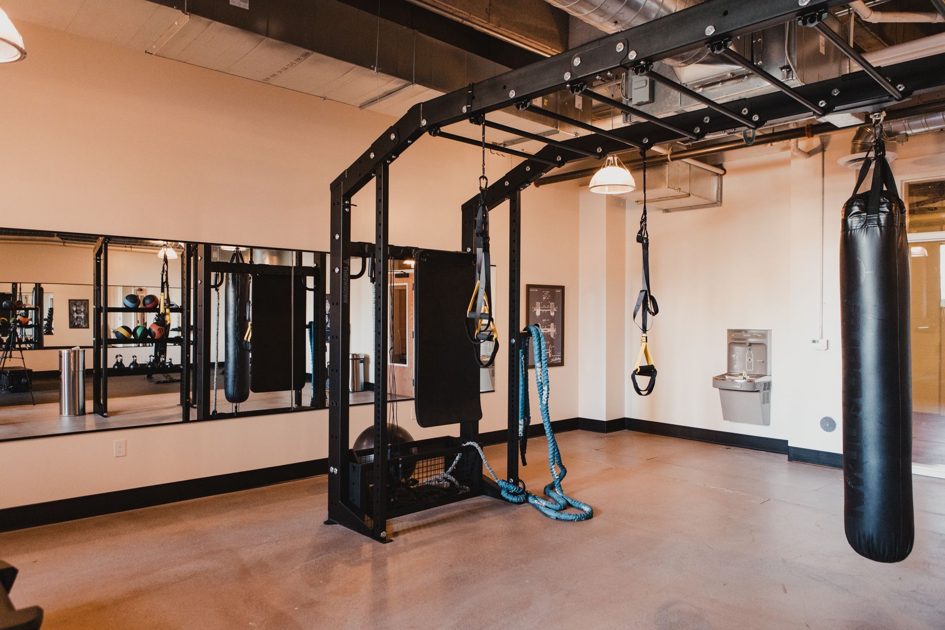 Gym with pull-up bars, punching bag, mirrors, and training equipment; light-colored walls and concrete floor at Zenith Apartments in Duluth, MN.