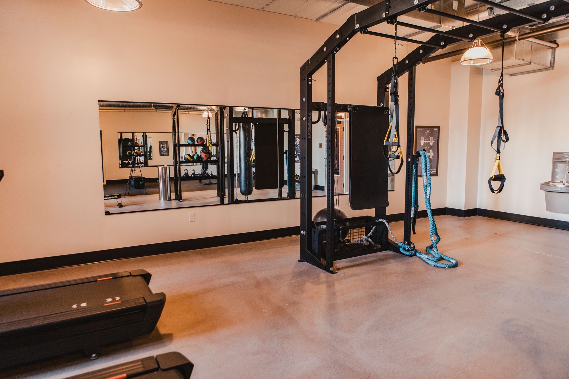 Gym with weight rack, mirrors, treadmill, and exercise equipment. Light brown walls, concrete floor at Zenith Apartments in Duluth, MN.