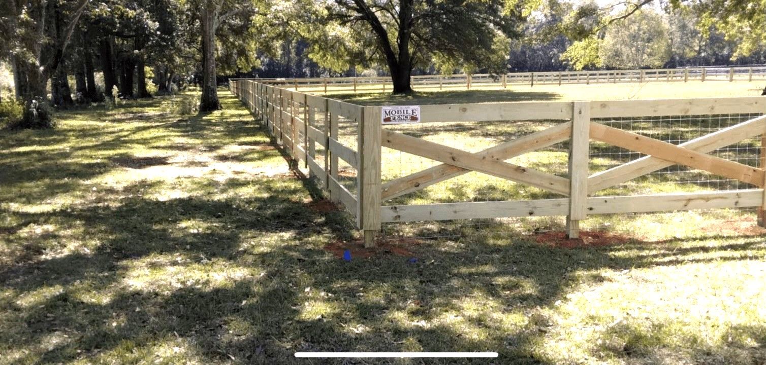 A white fence surrounds a grassy field with a house in the background A white fence surrounds a grassy field with a house in the background