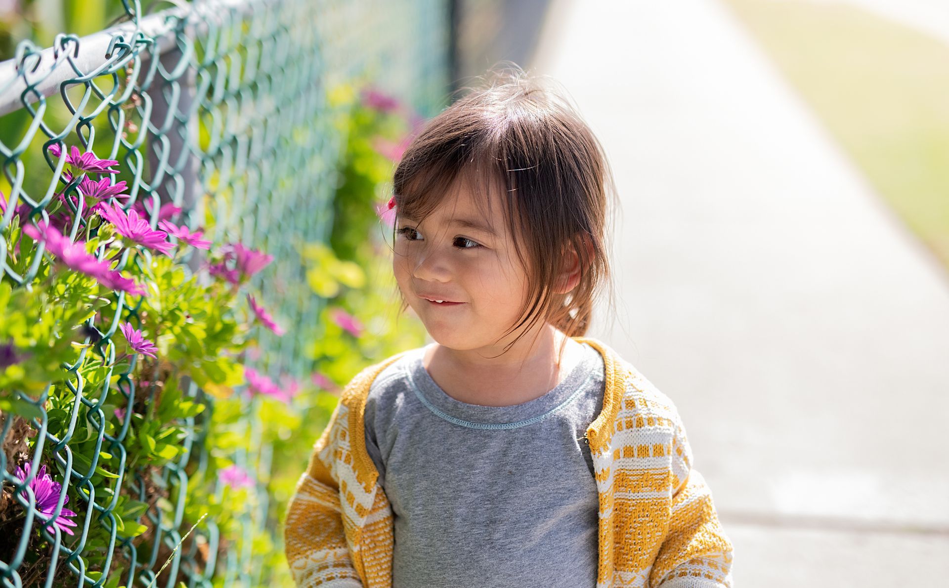 Young girl smiling beside a chain-link fence decorated with flowers, showcasing durable and attractive residential fencing by Mobile Fence Co. in Daphne, AL. Young girl smiling beside a chain-link fence decorated with flowers, showcasing durable and attractive residential fencing by Mobile Fence Co. in Daphne, AL.