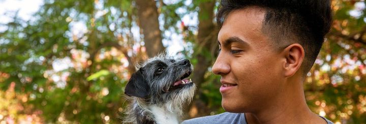 Man smiling at a small black-and-white dog outdoors with blurred trees in the background