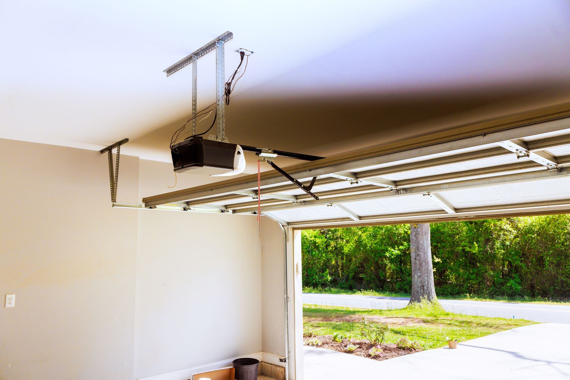 Open garage with raised door, ceiling opener, and driveway view of trees outside