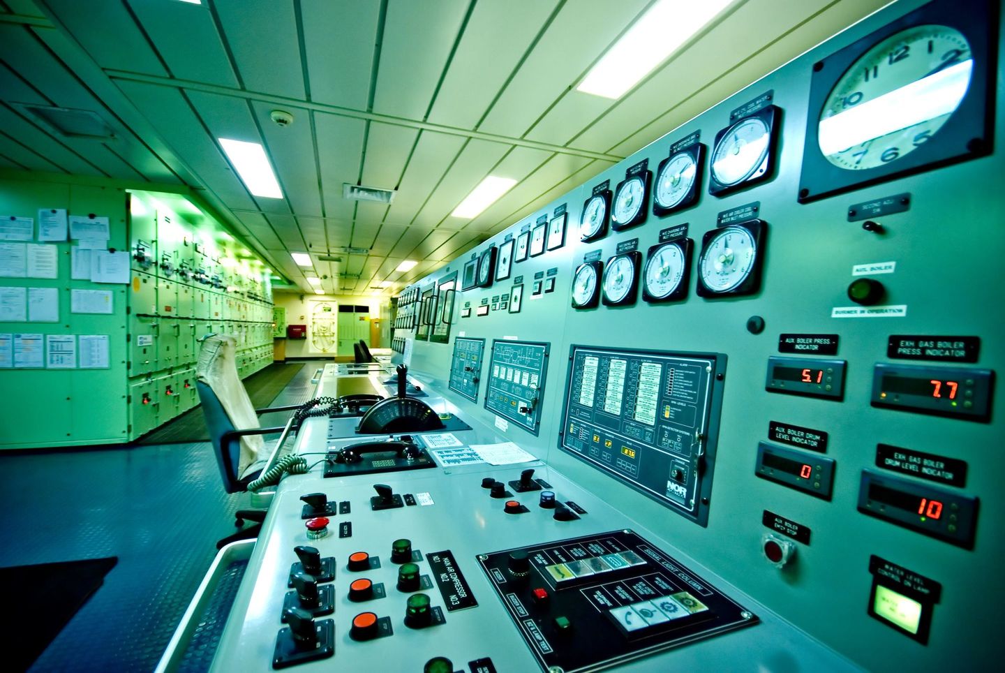 Control panel inside a ship's engine room, featuring gauges, screens, and various controls.