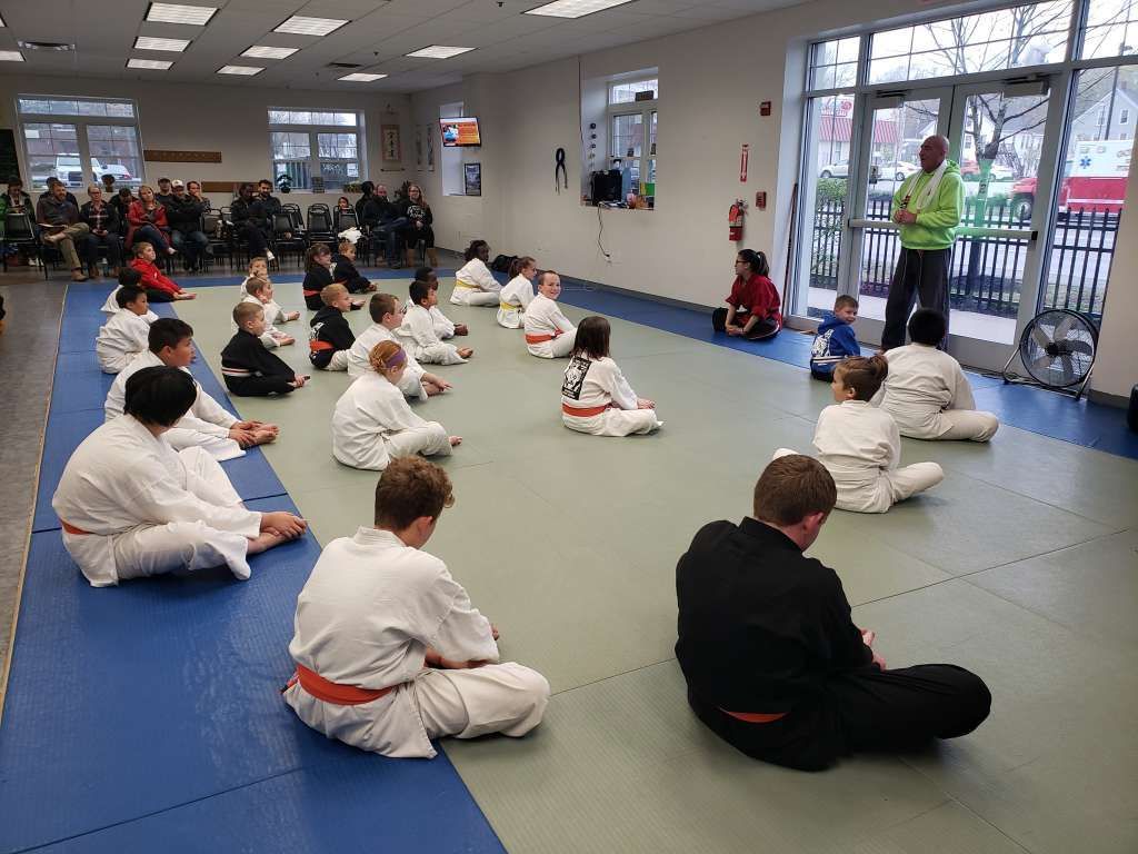 A group of children are sitting on the floor in a gym.