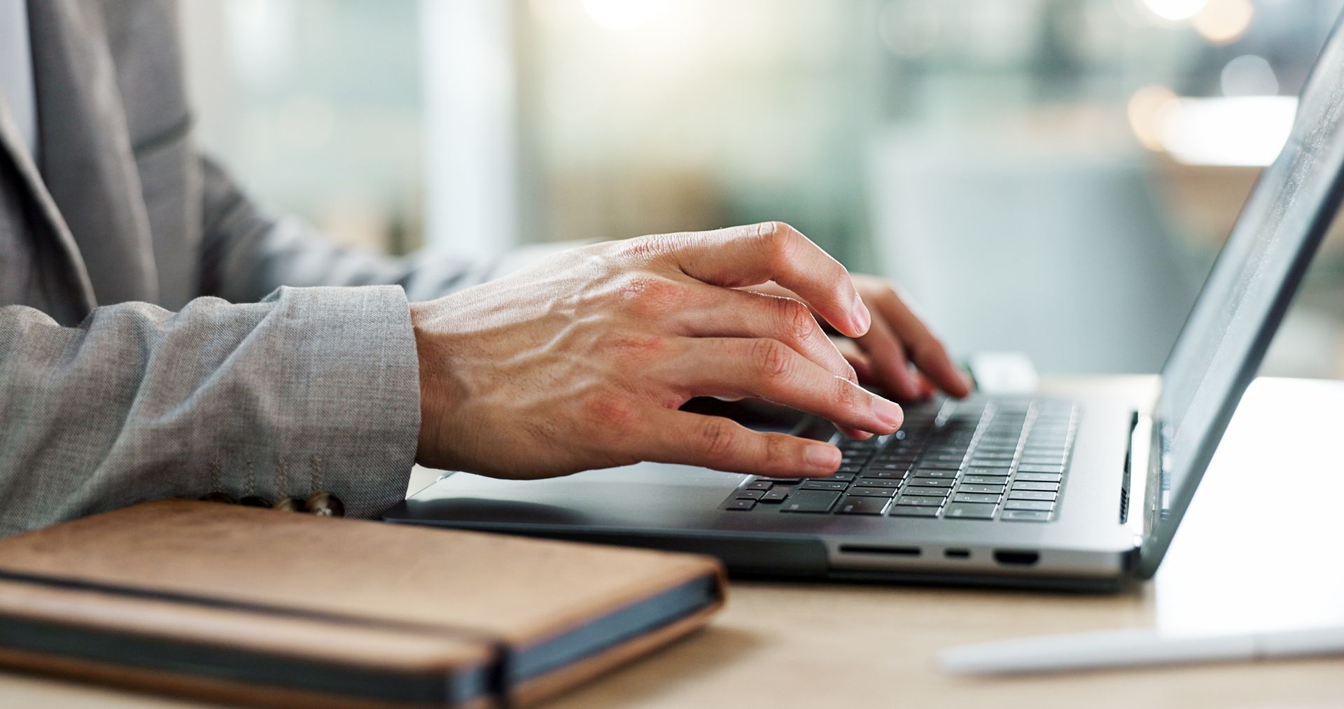 Hands typing on a laptop beside a notebook on a desk