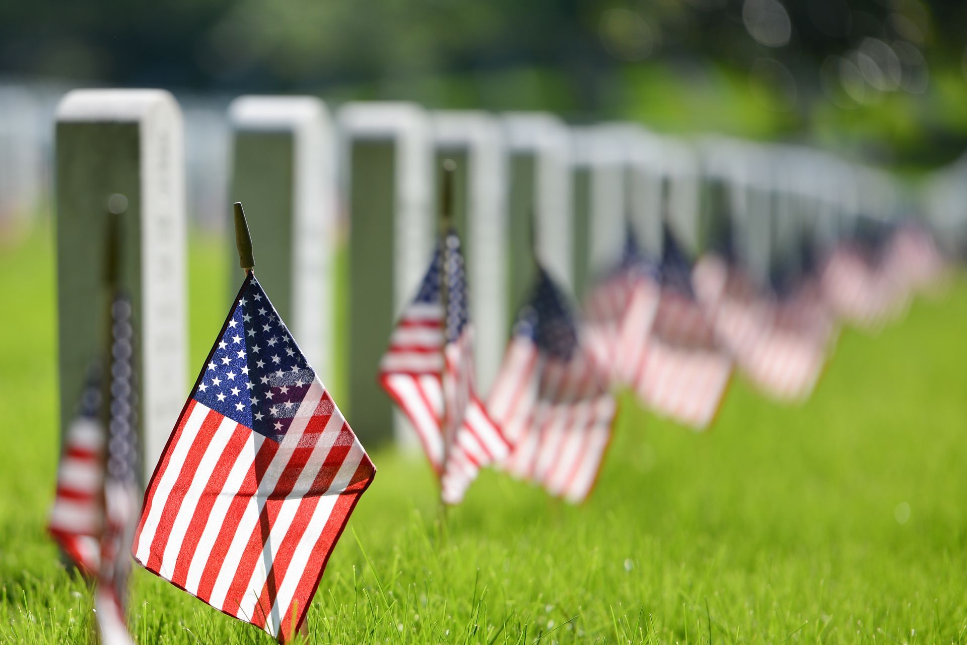 A woman is holding an american flag and a rose at a funeral.