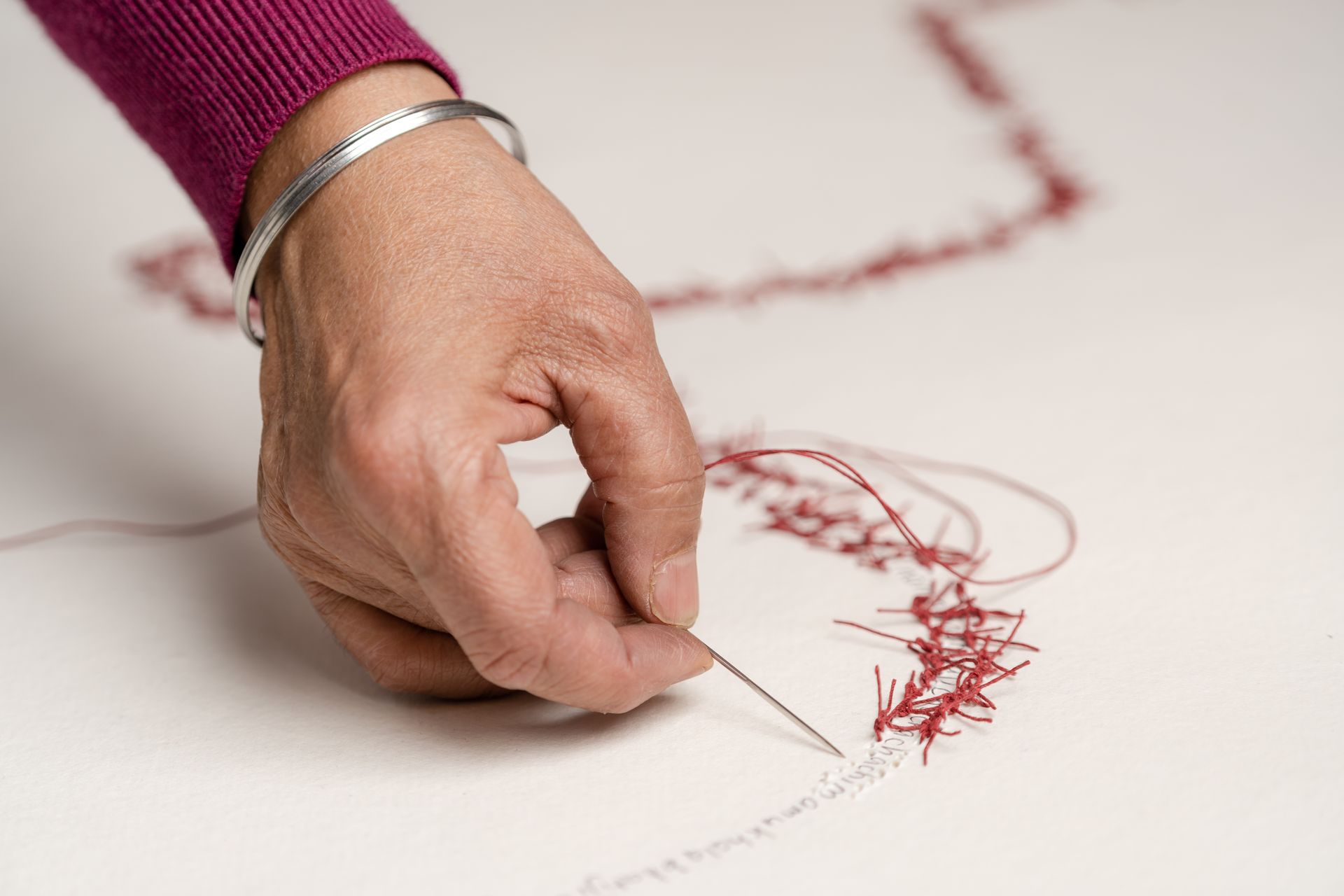 Hand stitching with red thread on white fabric.