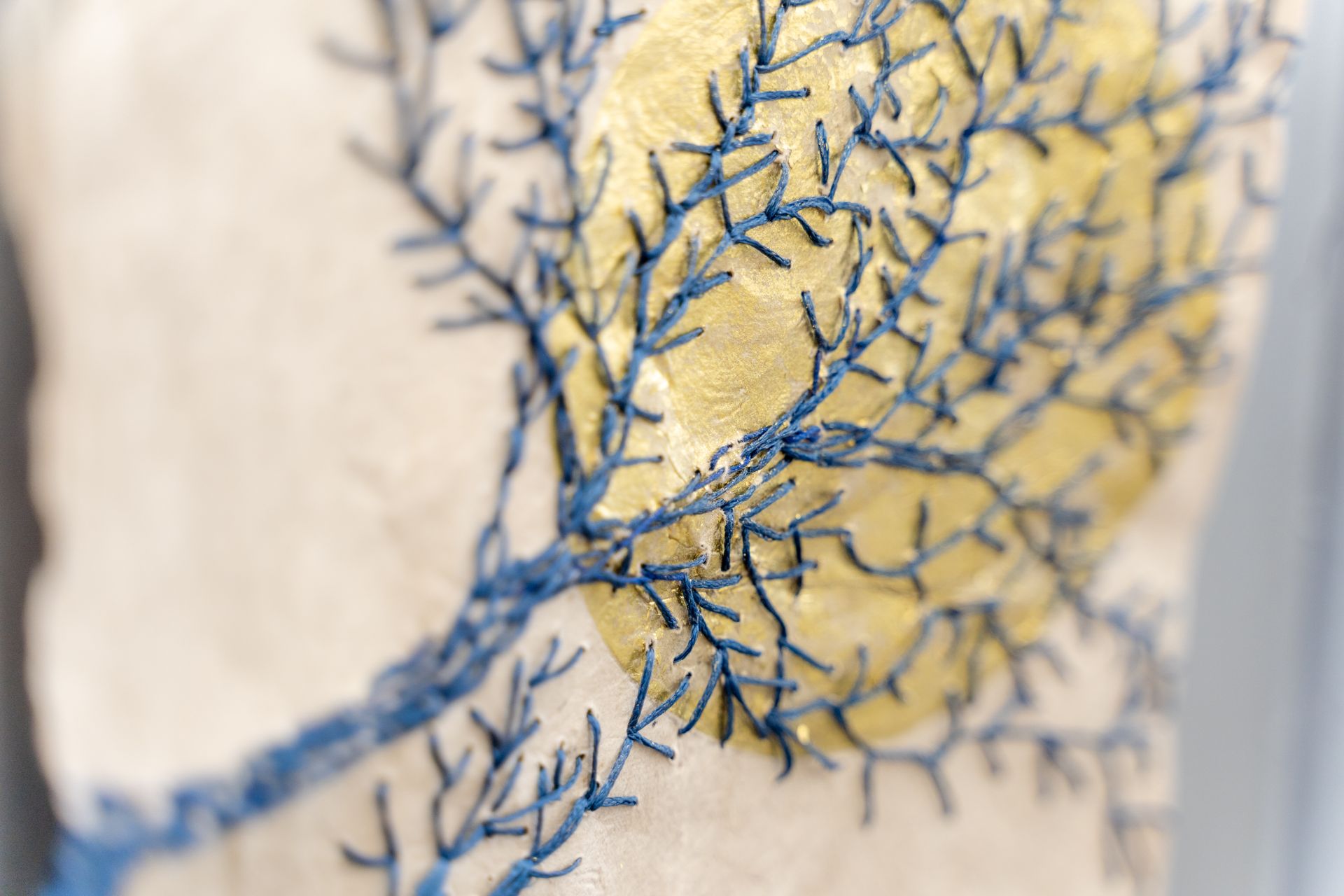 Close-up of cream fabric with blue embroidered tree branches and a gold foil sun.