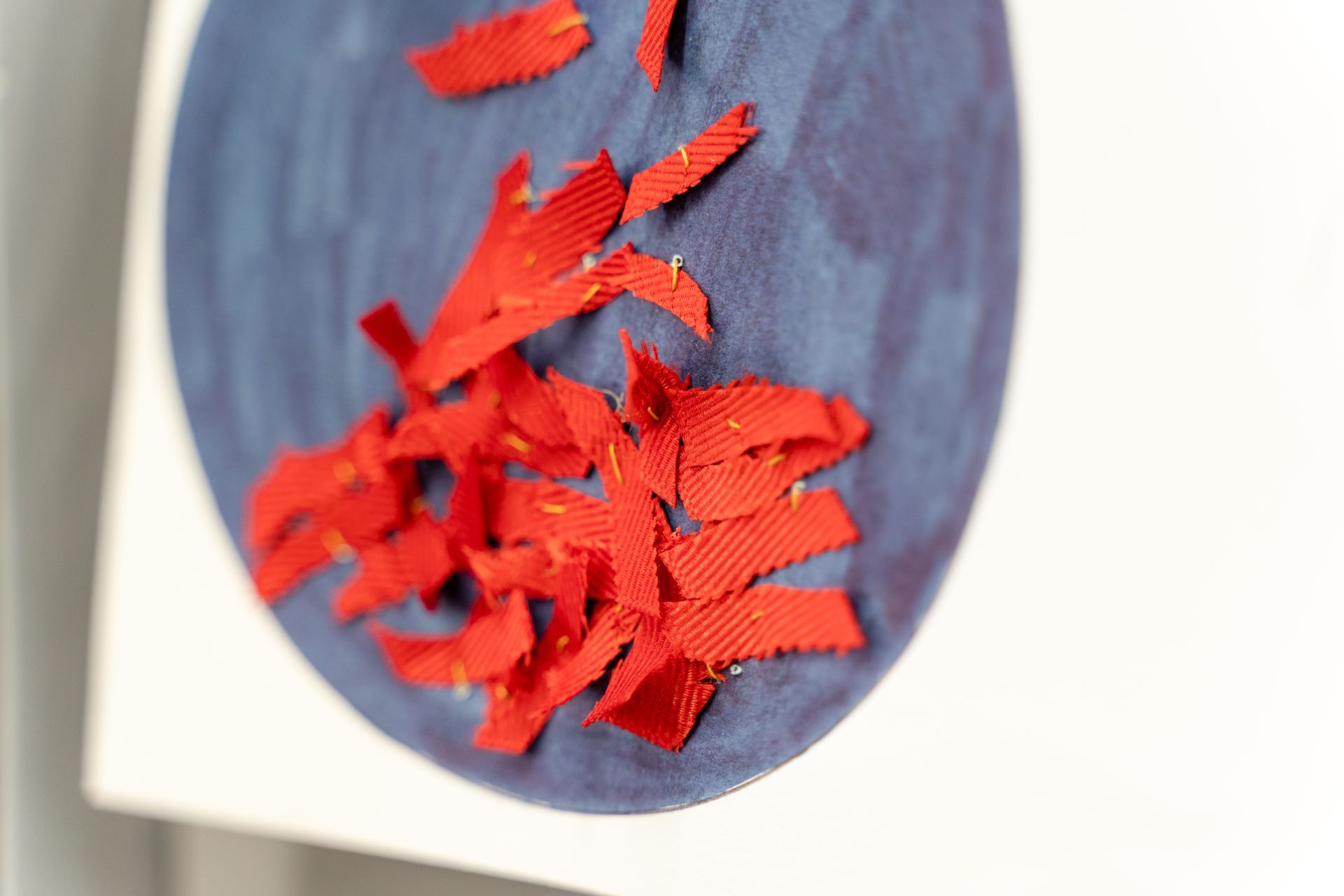 Close-up of a blue circle art piece with torn red paper pieces clustered on it.