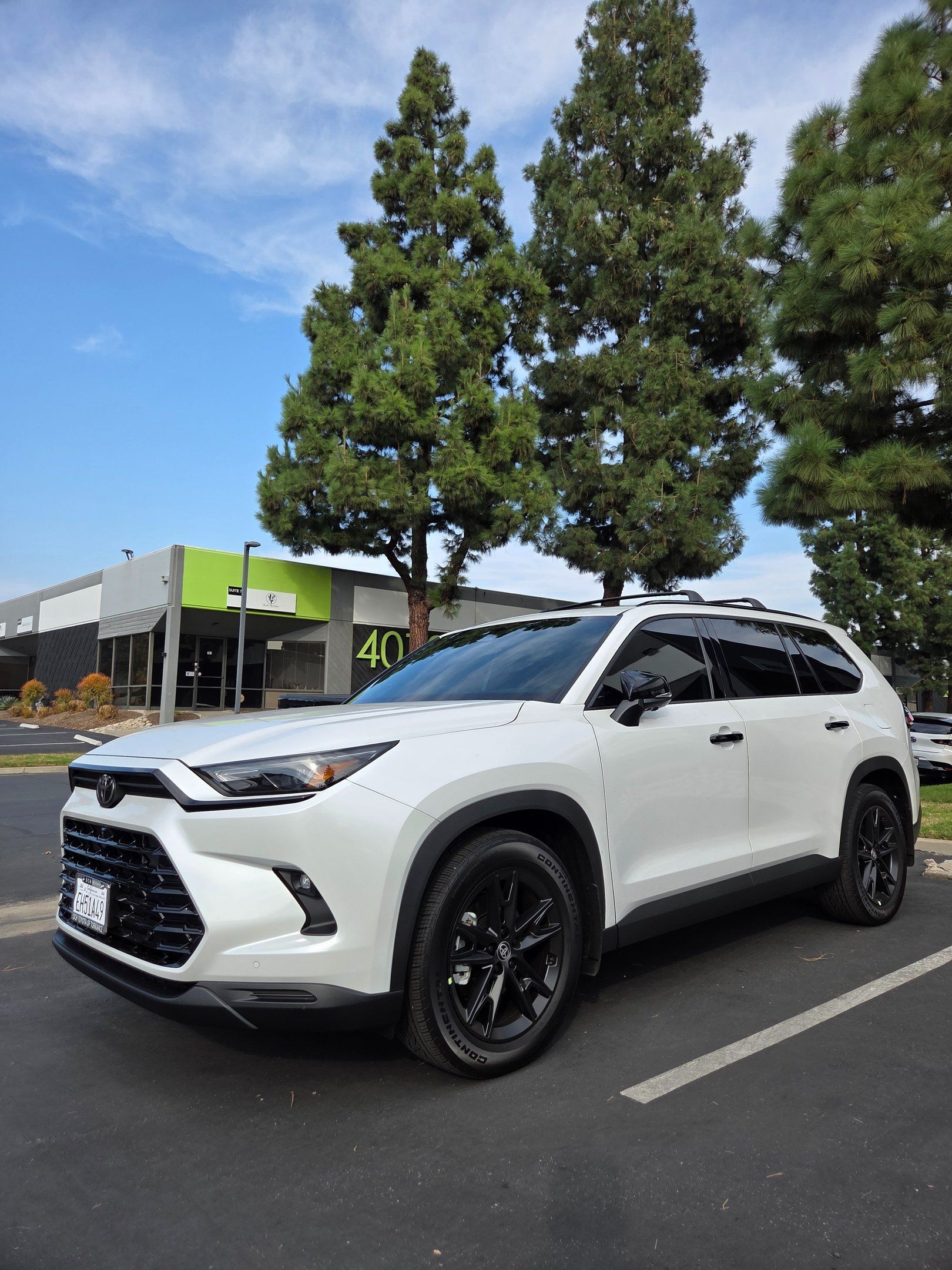 White SUV parked on a street with trees and a building in the background