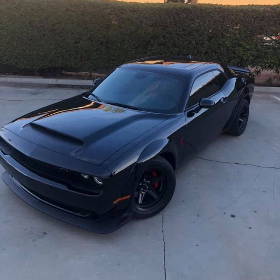 Black Dodge Challenger parked in a driveway at dusk, viewed from the front-left.