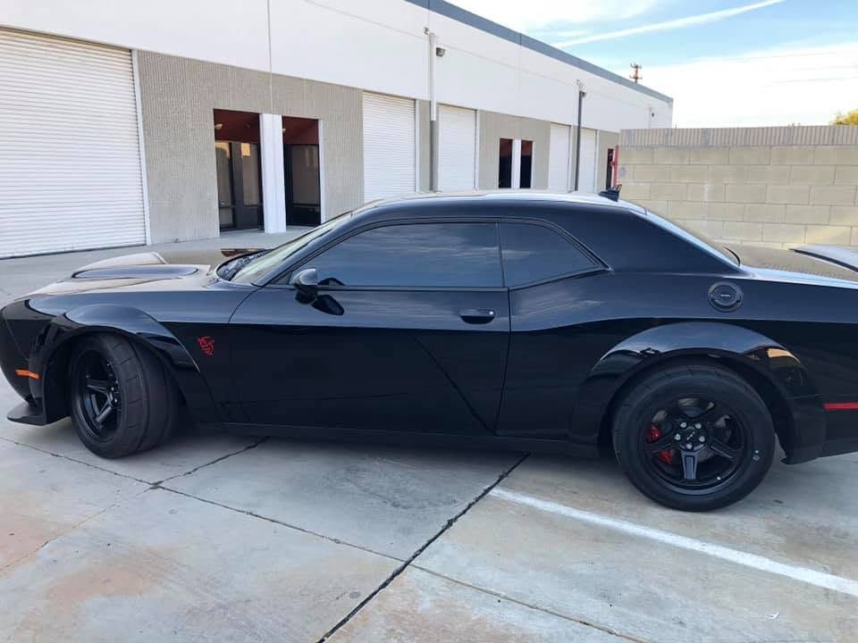 Black sports car parked outside a white industrial building.