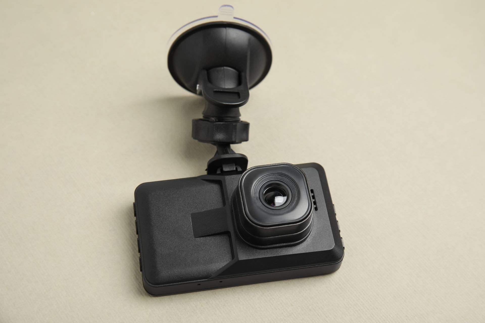 Black dashcam with suction-cup mount on a beige surface.