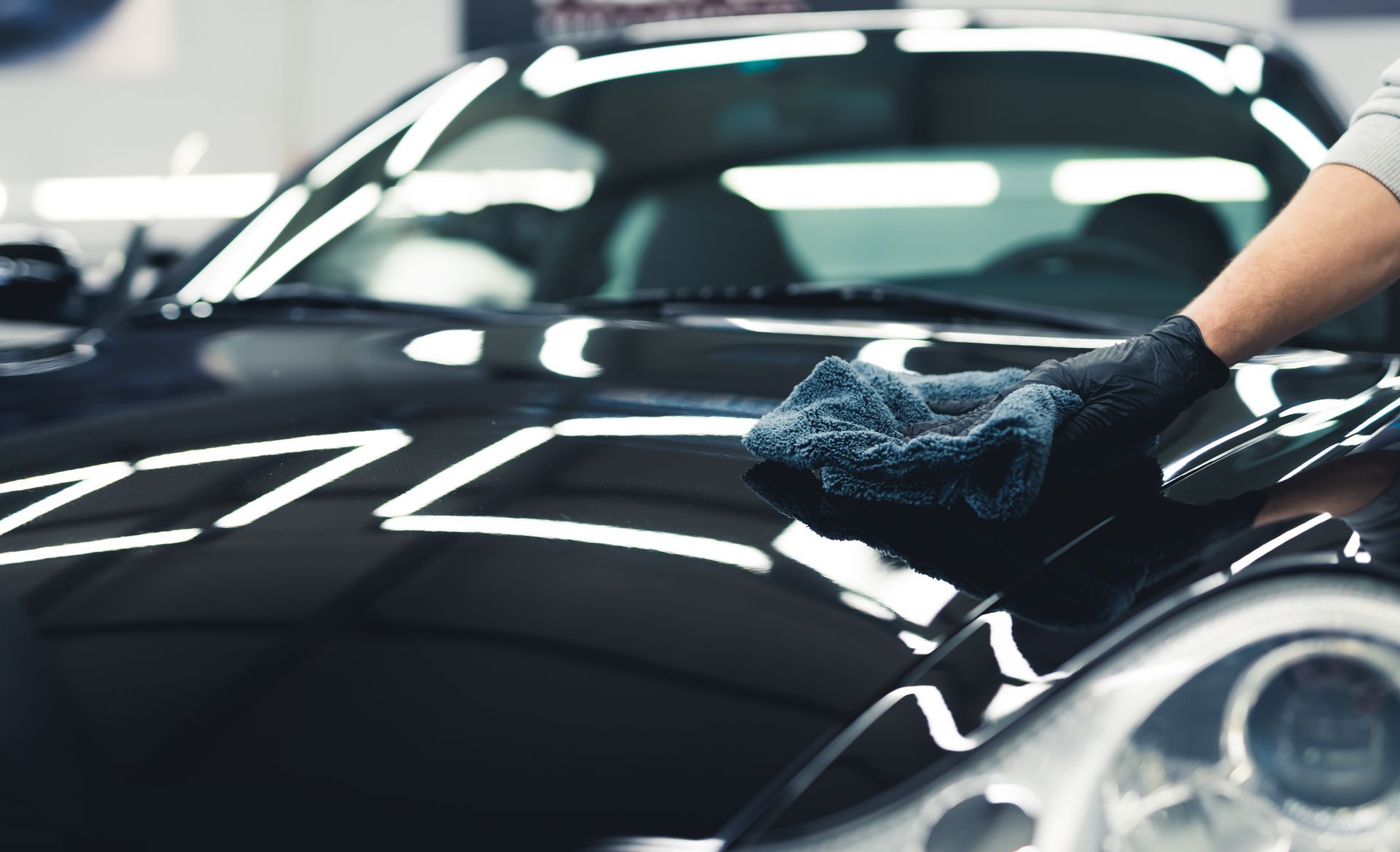 Gloved hand wiping the hood of a black car in a bright auto detailing shop Gloved hand wiping the hood of a black car in a bright auto detailing shop