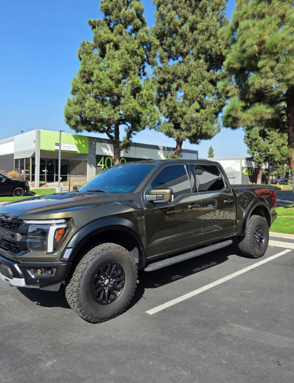Black lifted pickup truck parked in a lot with trees and a building in the background