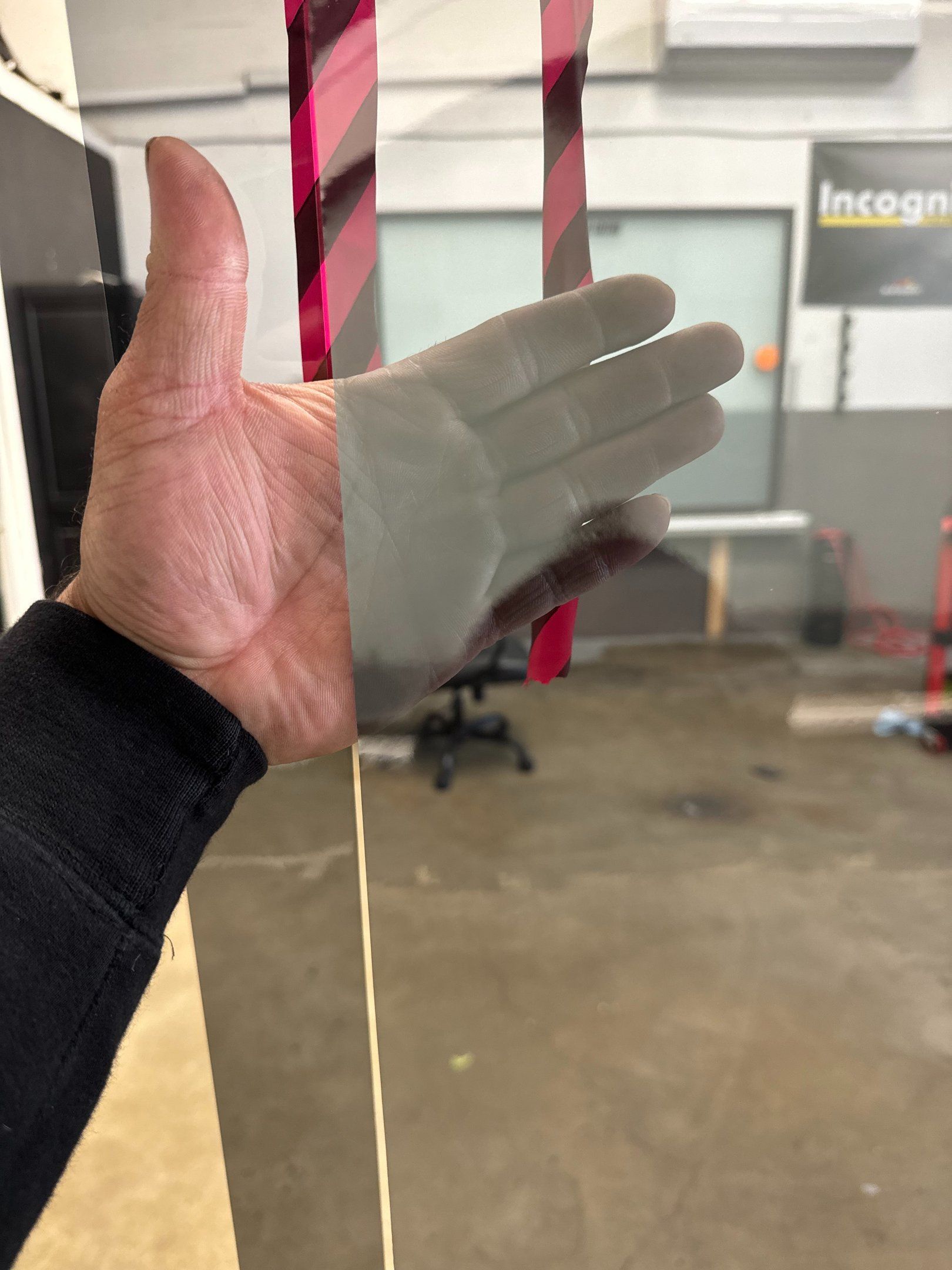 Hand with black sleeve and translucent glove held up in front of a glass door with pink stripes