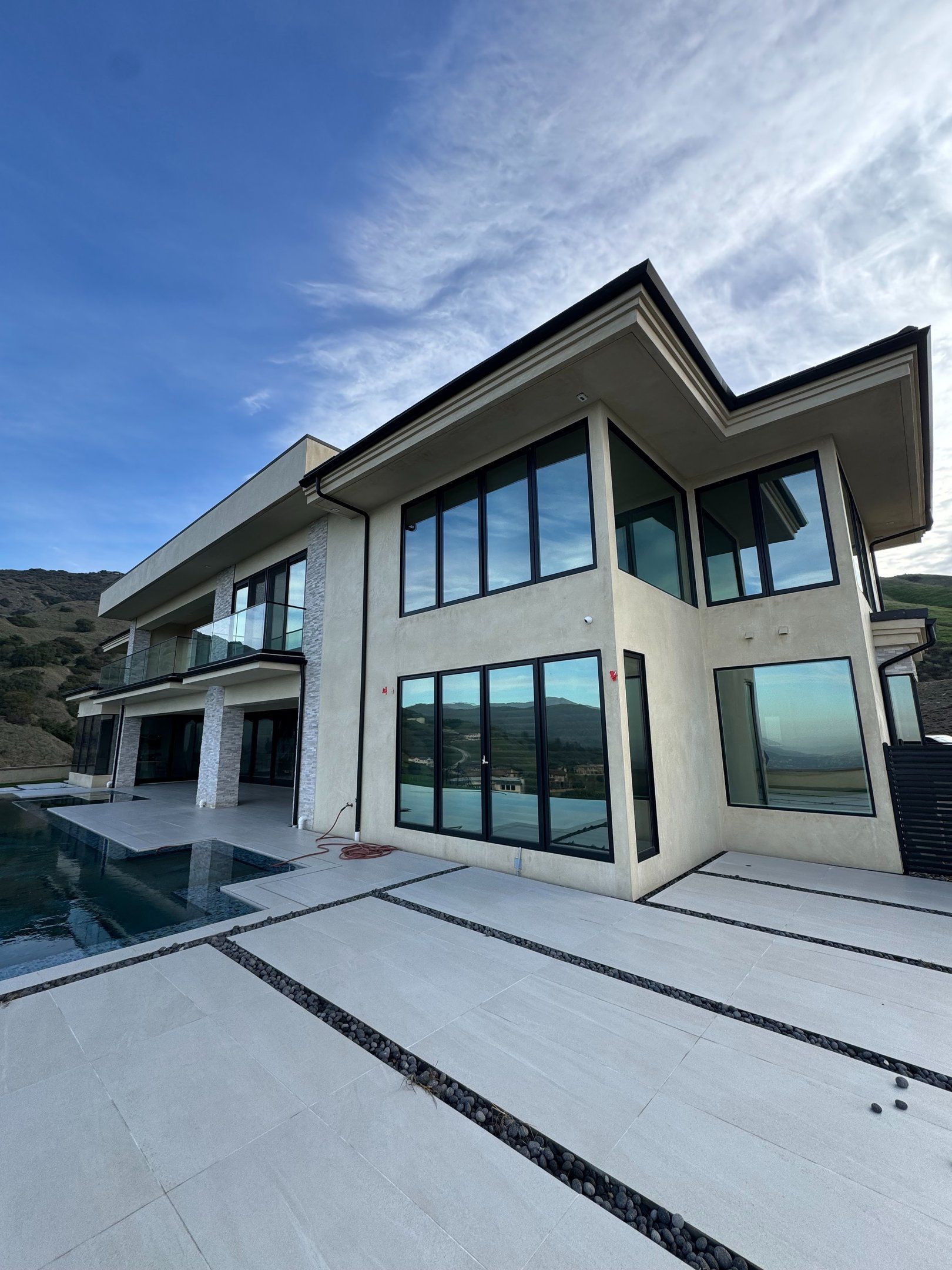 Modern two-story luxury house with large windows, poolside patio, and mountain view under a blue sky