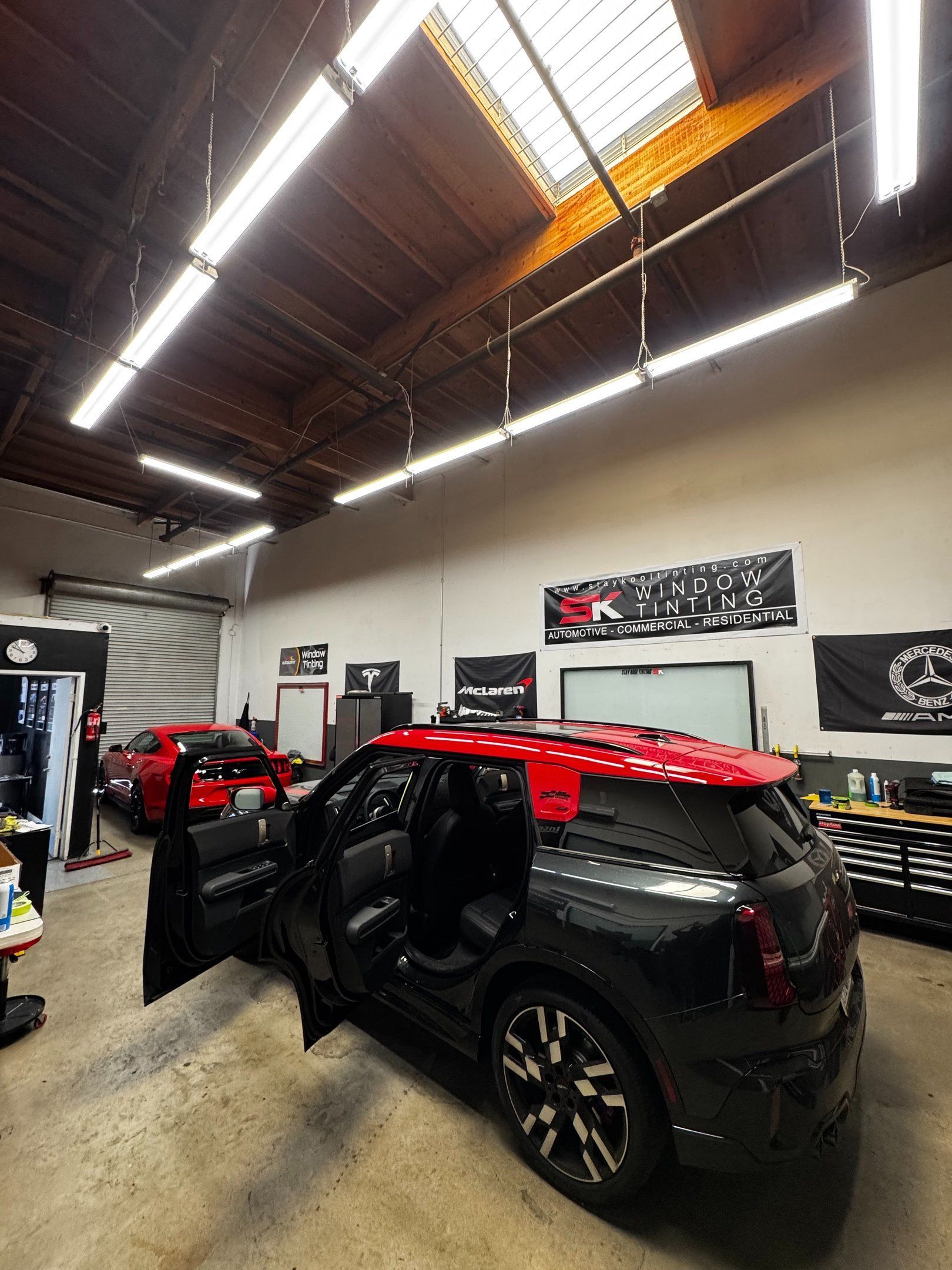 Black SUV with red accents in a garage workshop, doors open under bright overhead lights.