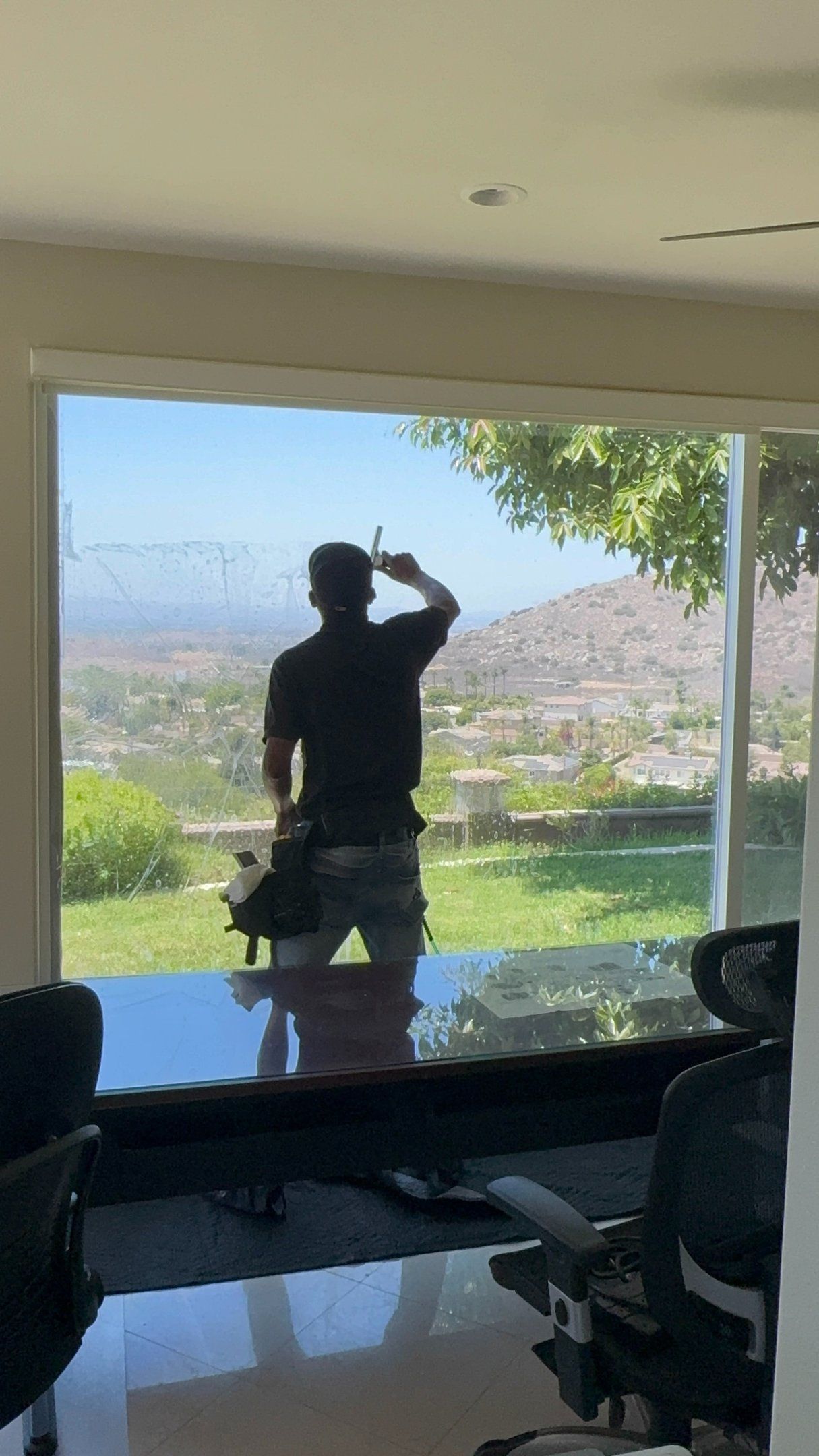 Person silhouetted by a large window, looking out over a city and hillside view.