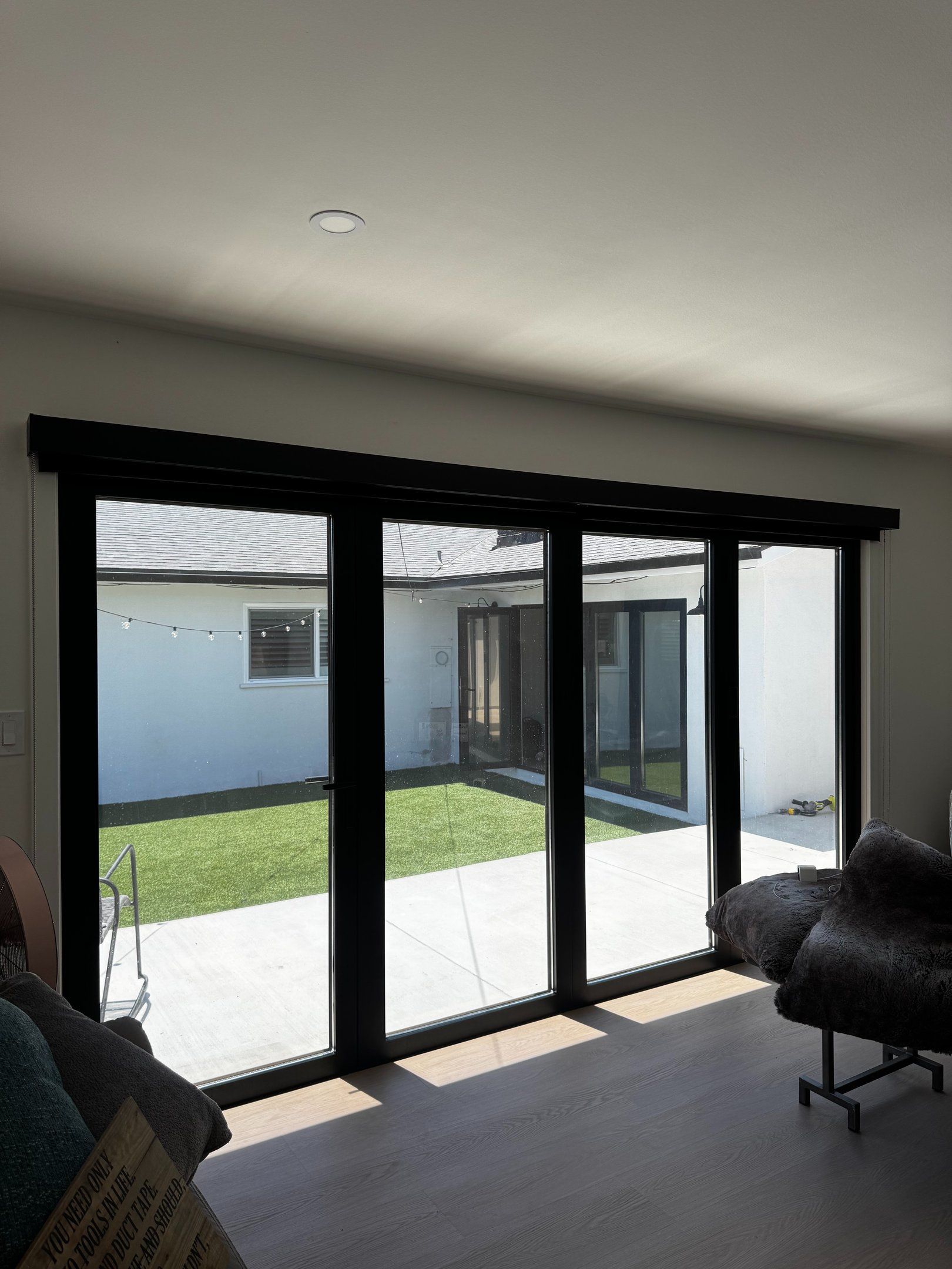 Modern living room with black-framed sliding glass doors opening to a sunny courtyard and lawn