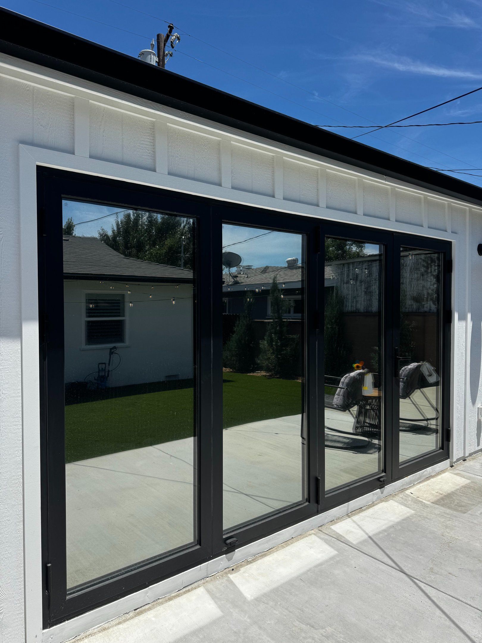 Modern house exterior with black-framed glass sliding doors and a patio facing a green backyard