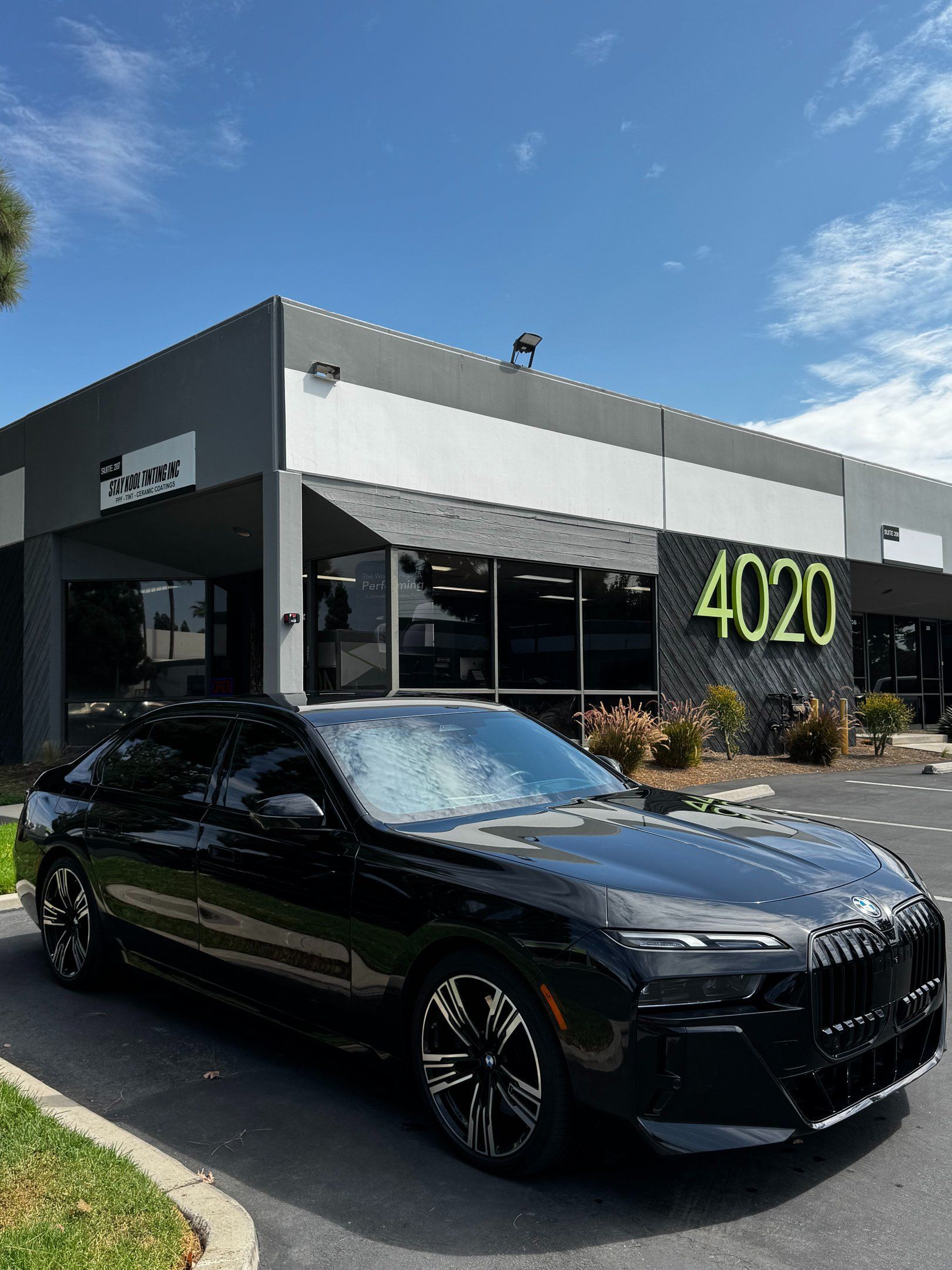 Black luxury sedan parked outside a modern building with “4020” on the facade