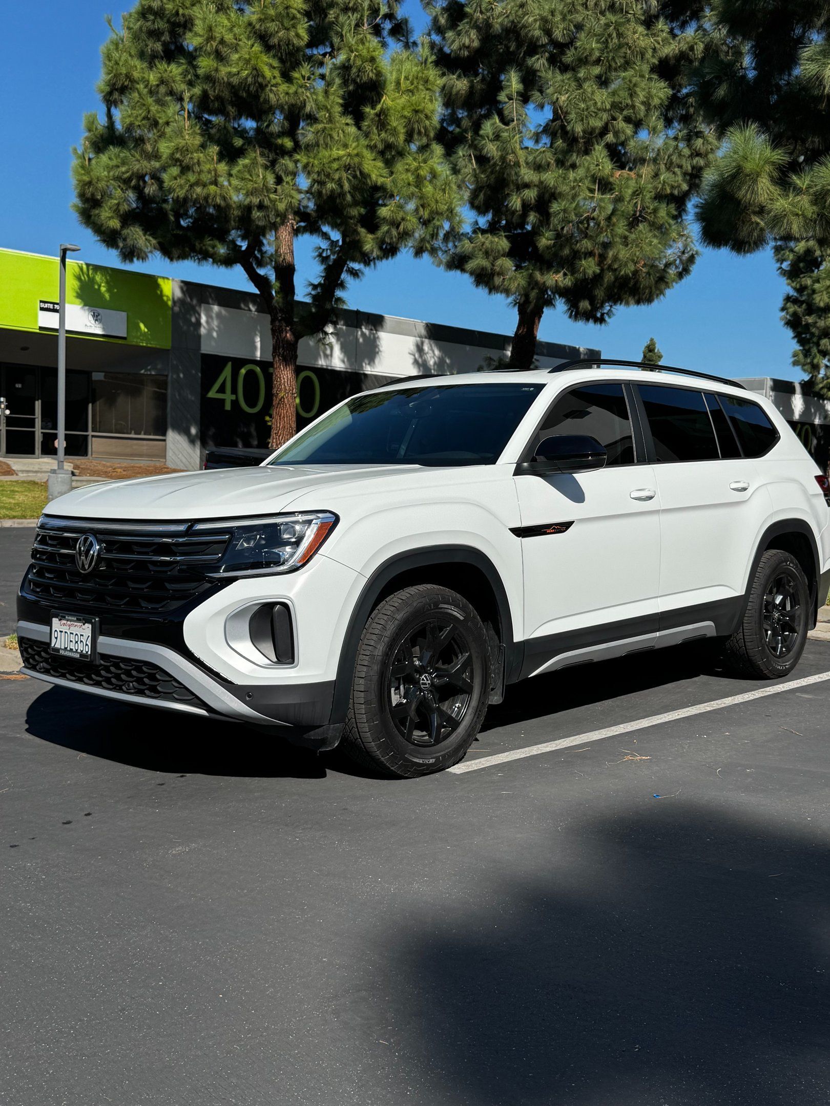 White SUV parked in a lot beside a building and tree on a sunny day