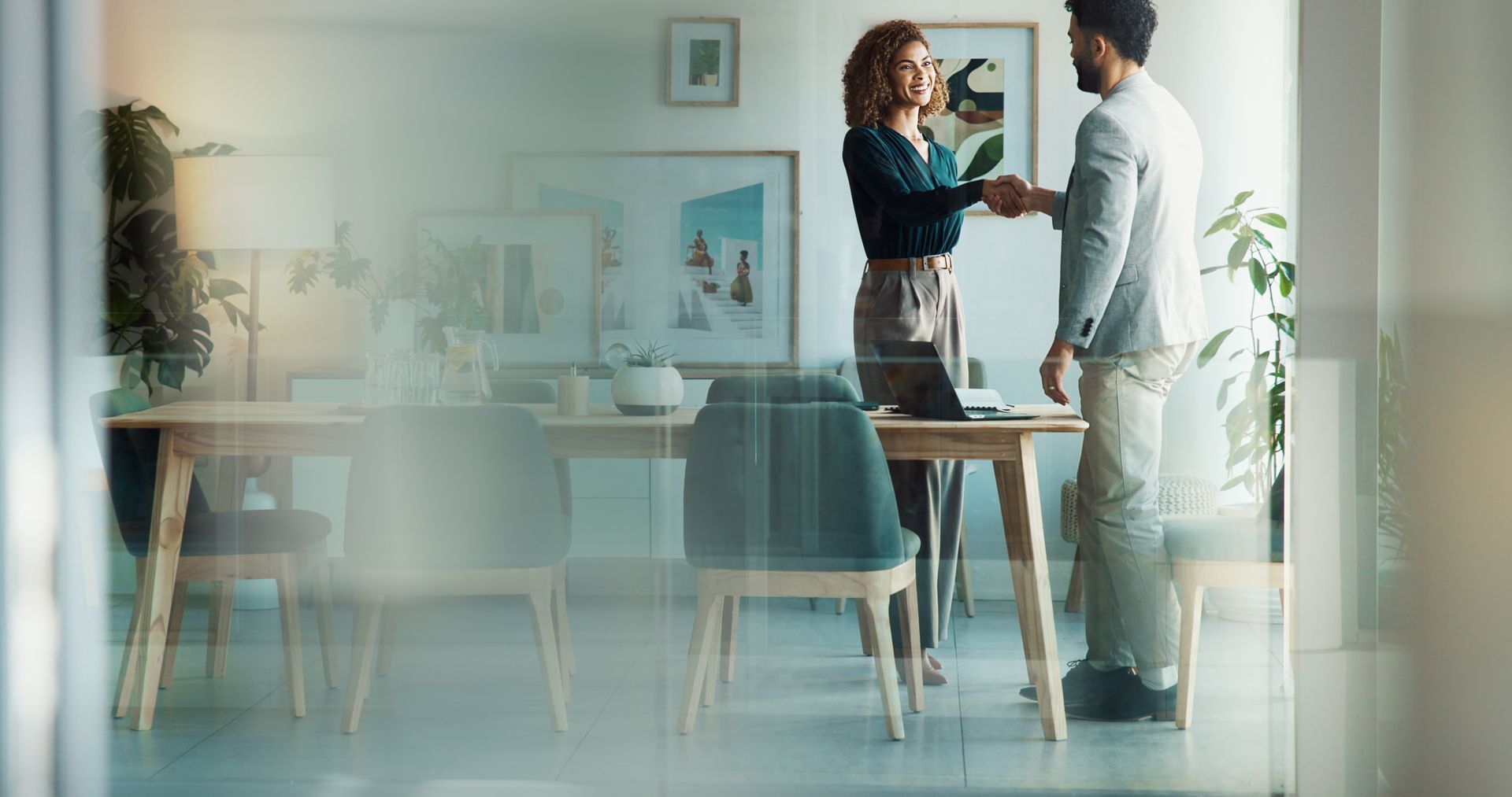 Two people shaking hands in a modern office setting, celebrating a deal or agreement.