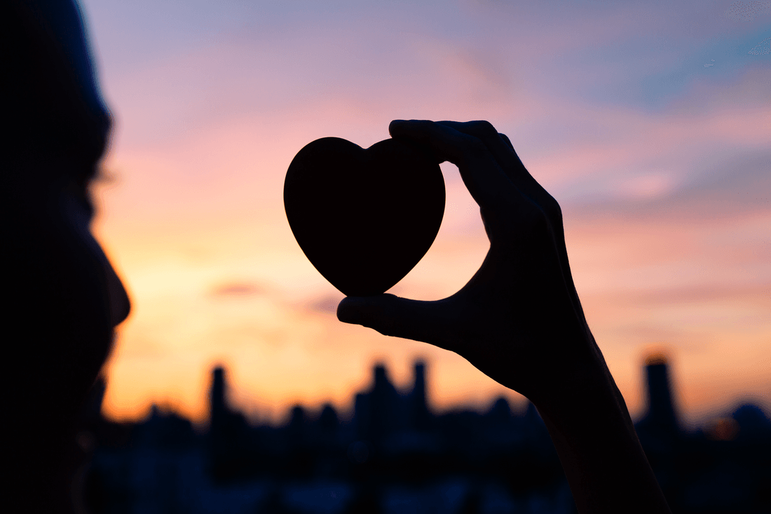A person is holding a heart in their hand at sunset