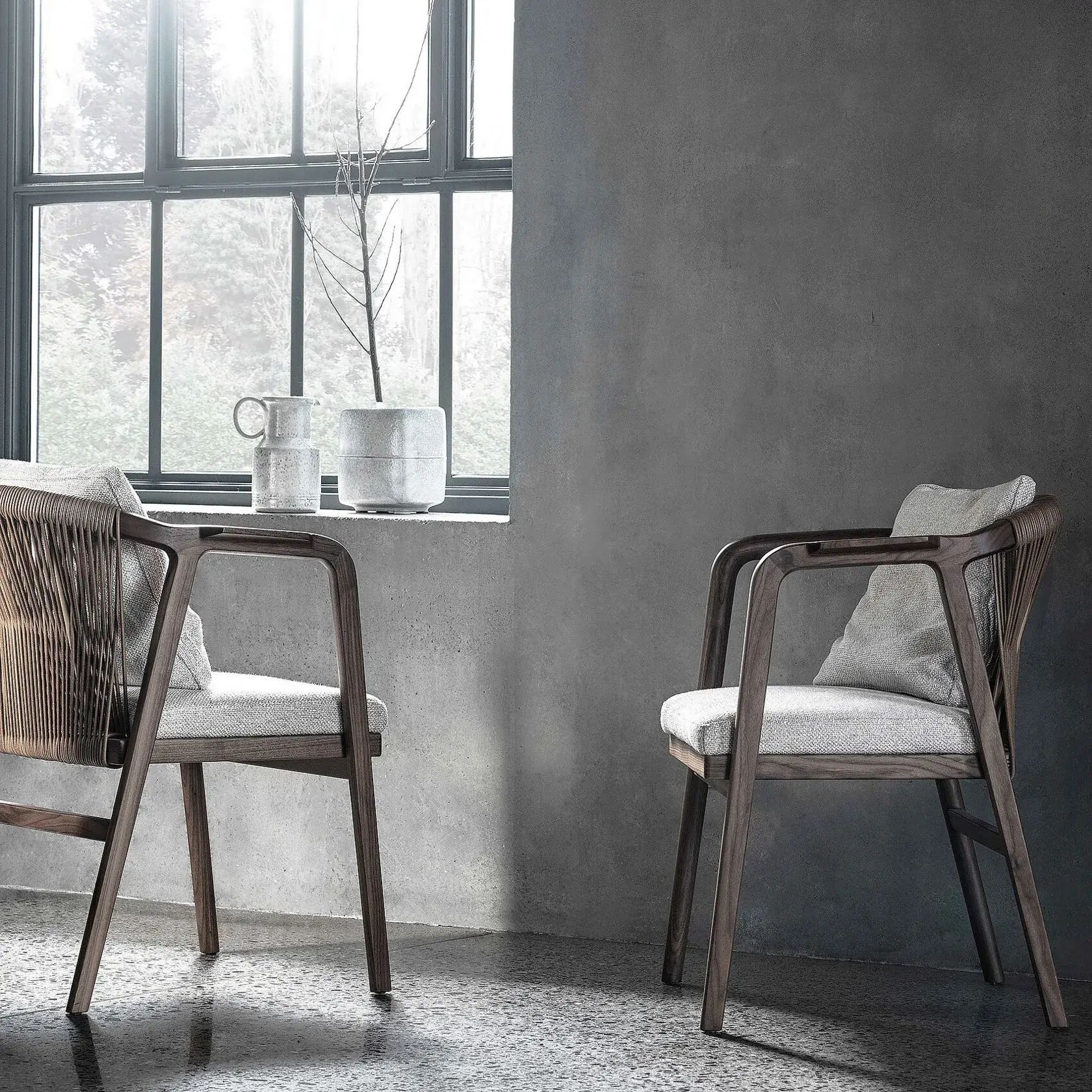 Dos sillas de madera junto a una gran ventana en una habitación minimalista de color gris.