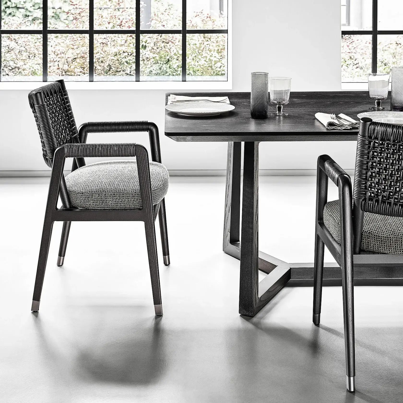 Mesa de comedor moderna con sillas de mimbre en una habitación luminosa y minimalista junto a grandes ventanales.